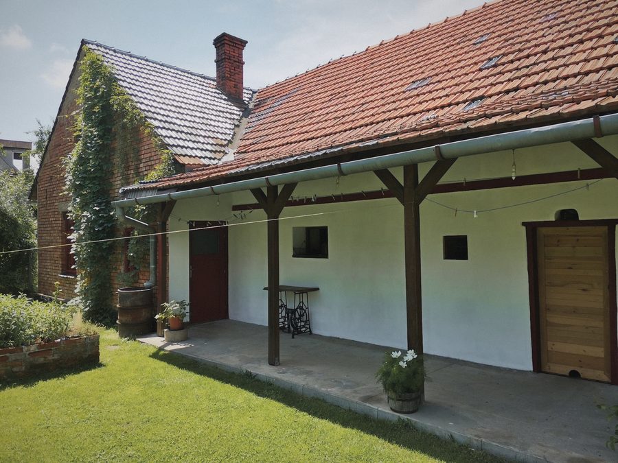 Bílá pavlač s červenými sloupky, dřevěné dveře a květiny