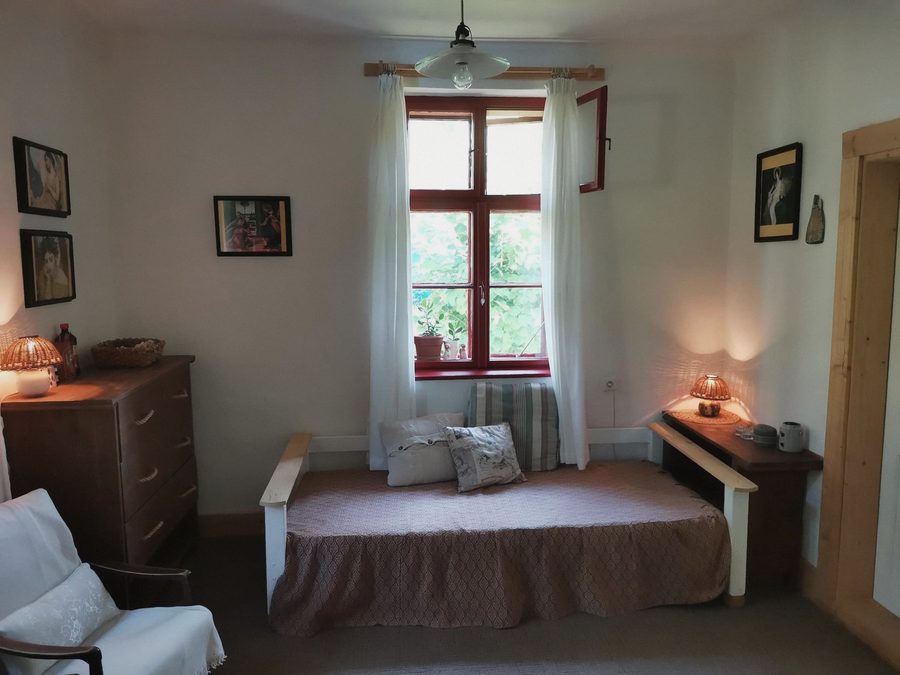 Pokoj s rozkládací postelí, komodou a oknem s červeným rámem