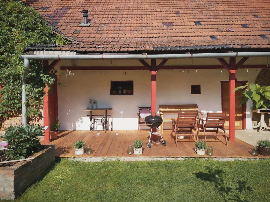 Krytá dřevěná veranda s červenými sloupky, stolem, křesly a grilem
