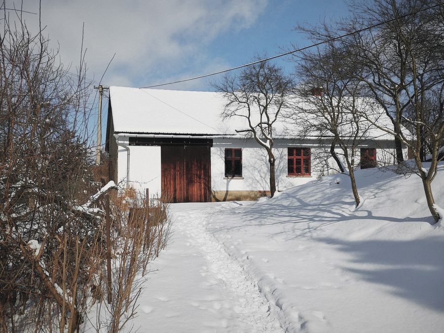 Zasněžená cesta k bílé stodole s dřevěnými vraty